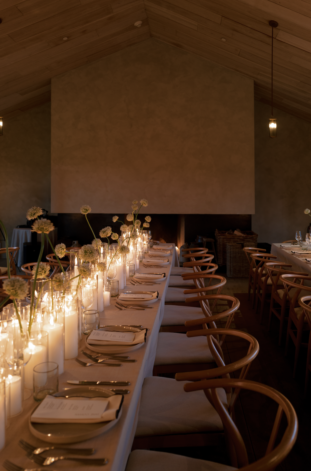 Elegant dinner table set with candles, glasses, and flowers in a warmly lit room with wooden ceiling.