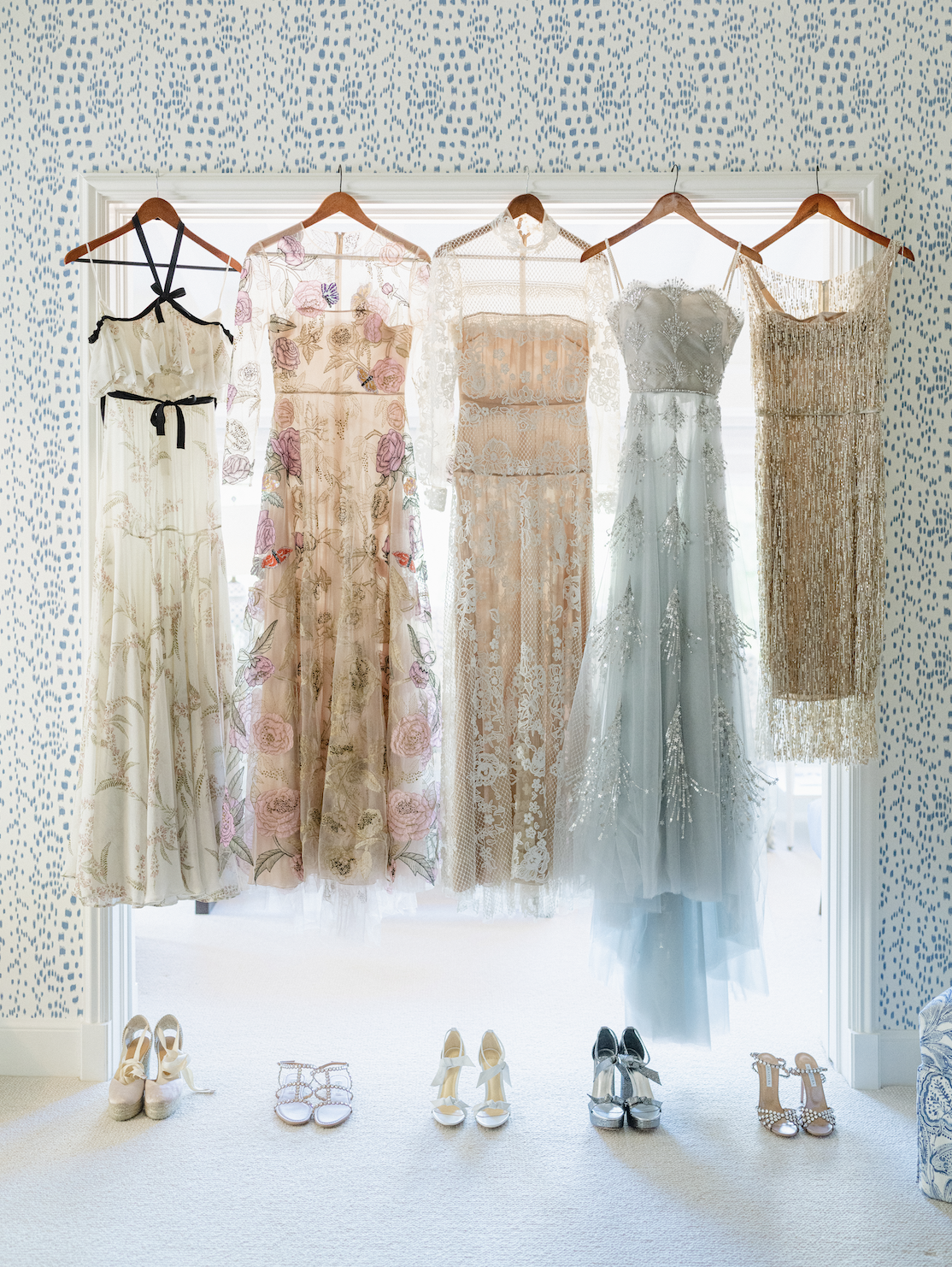 Five dresses hanging on a window, with six pairs of shoes placed below.