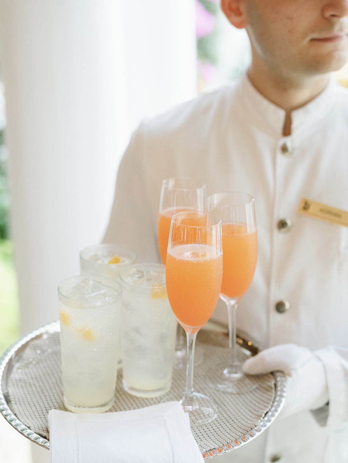 A server holding a tray with glasses of orange and lemon drinks, some with lemon slices, at an event or restaurant.