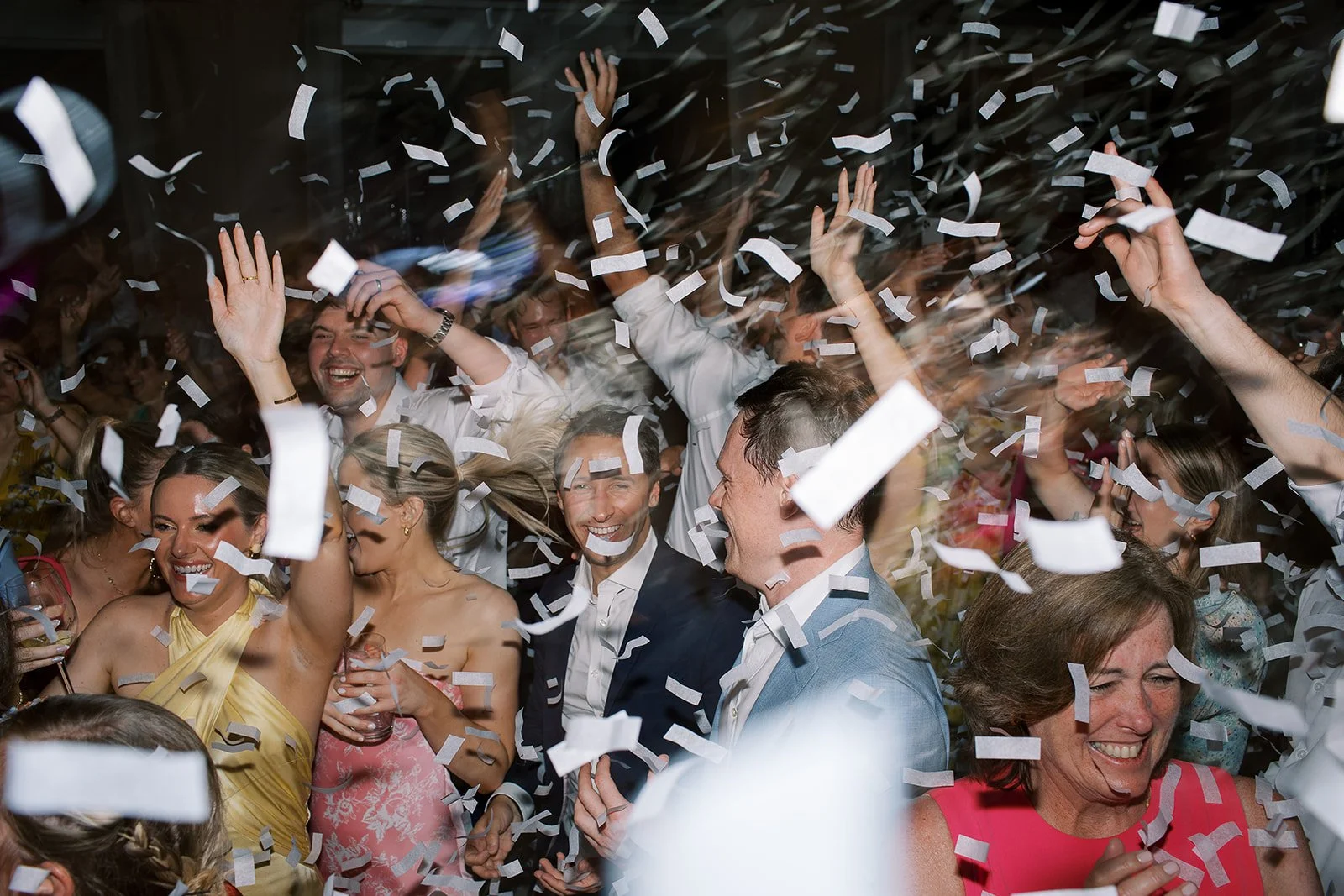 People celebrating at a party with confetti falling down, smiling, dancing, and enjoying the moment.