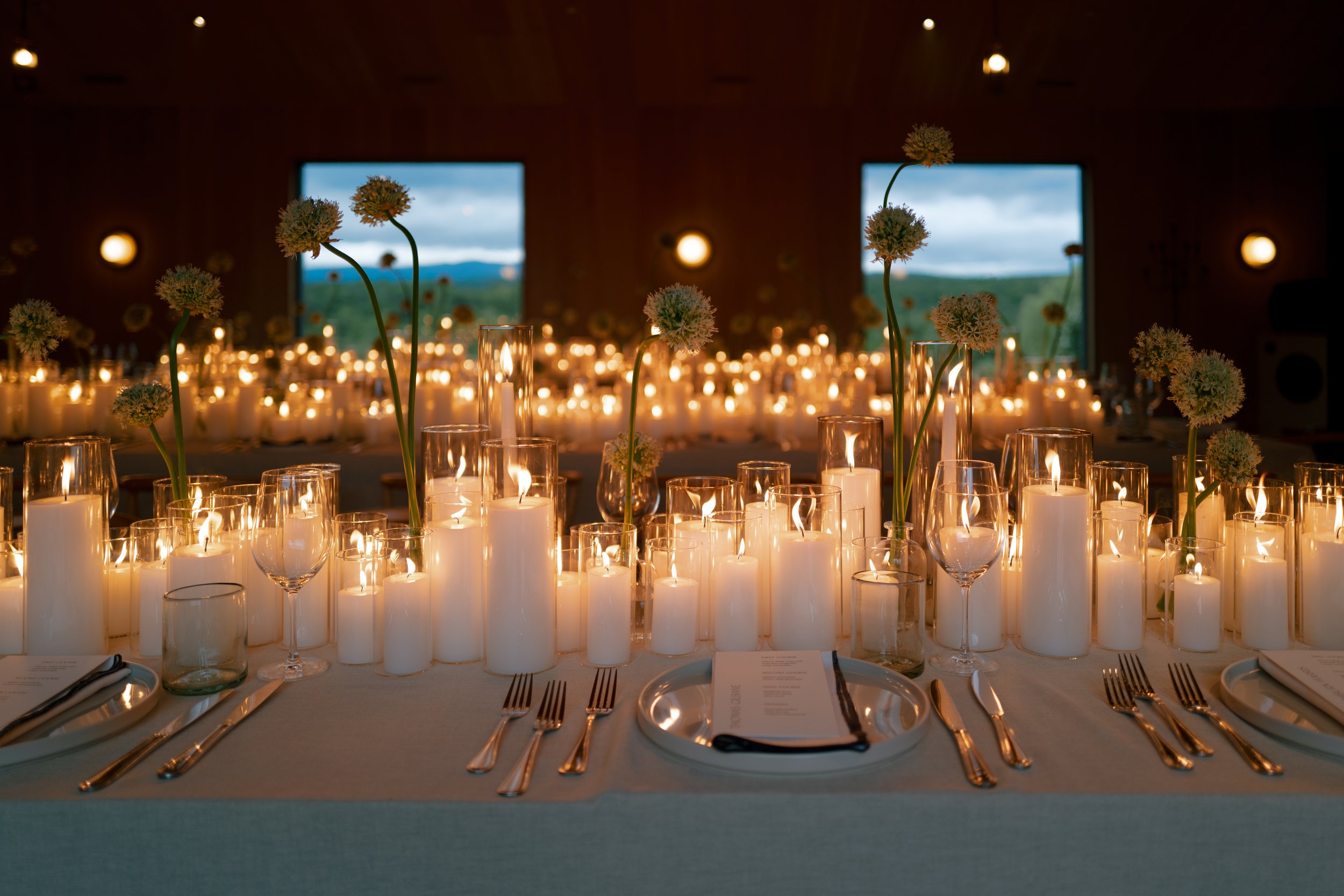 A decorated dinner table at sunset with candles, glassware, and floral centerpieces.