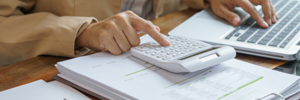 Person using a calculator and a laptop at a desk with papers.