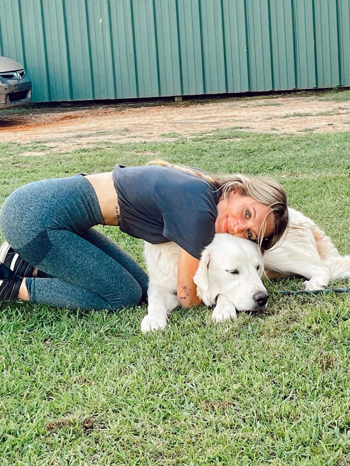 A woman hugging a large white dog lying on the grass.