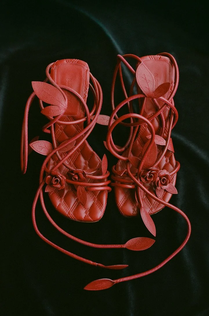 Red sandals adorned with 3D floral and leaf embellishments, placed on a dark surface.