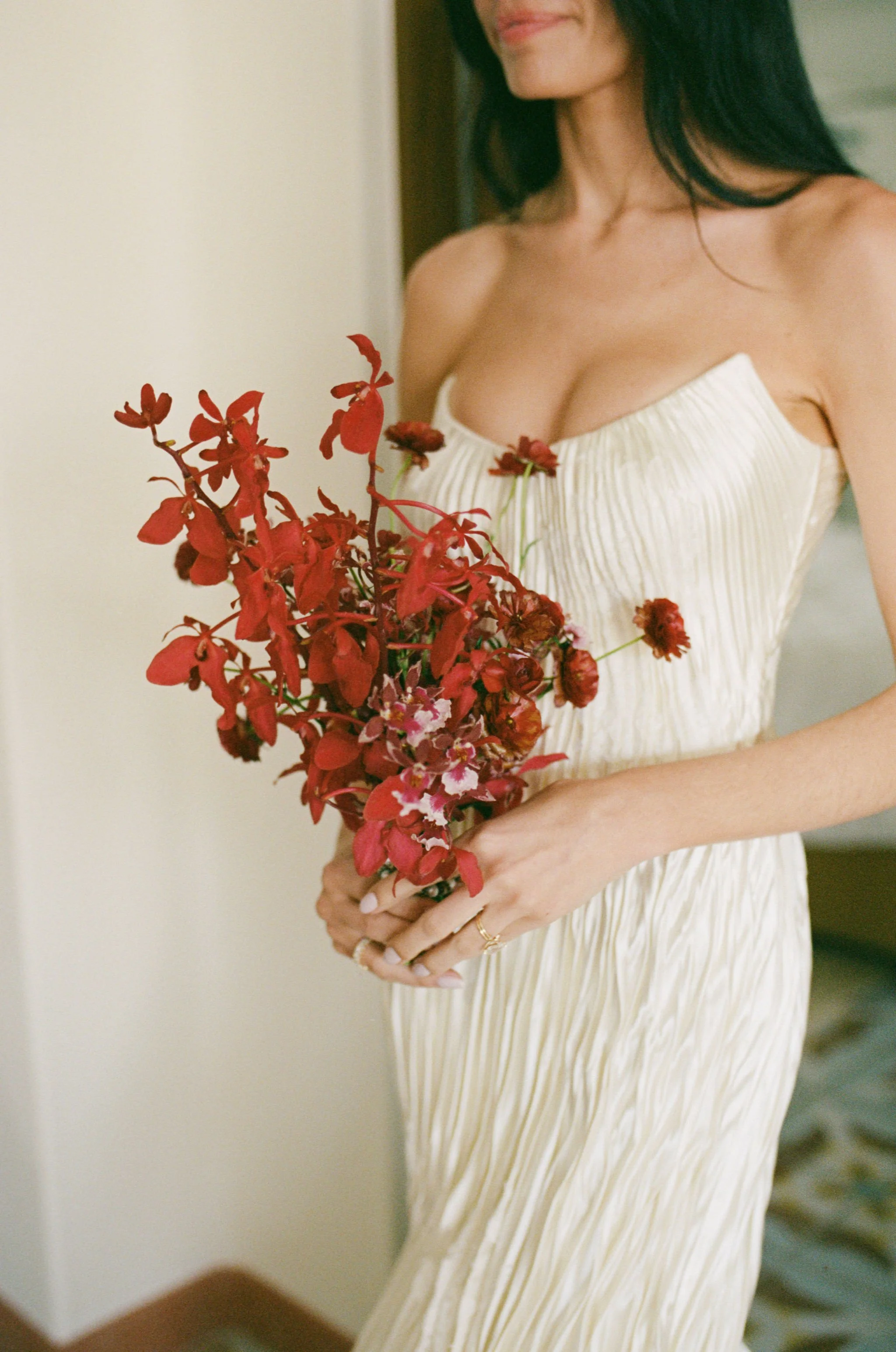 A woman holding a bouquet of red and pink flowers, wearing a white pleated dress.