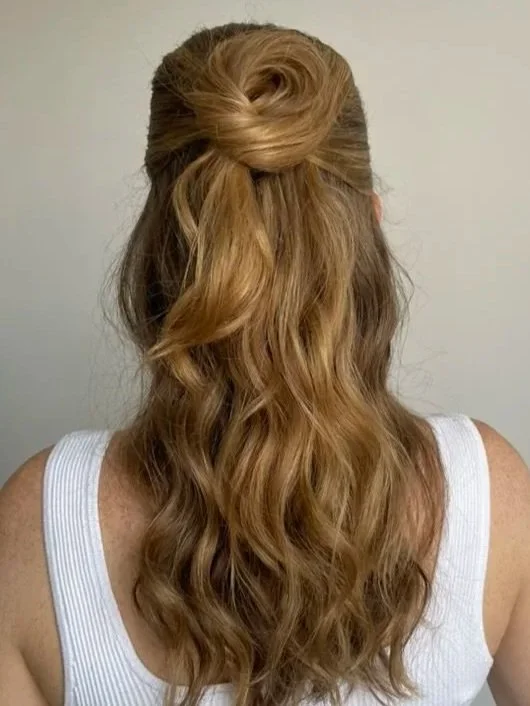 Back view of a woman with long, wavy, light brown hair styled with a half-up bun.