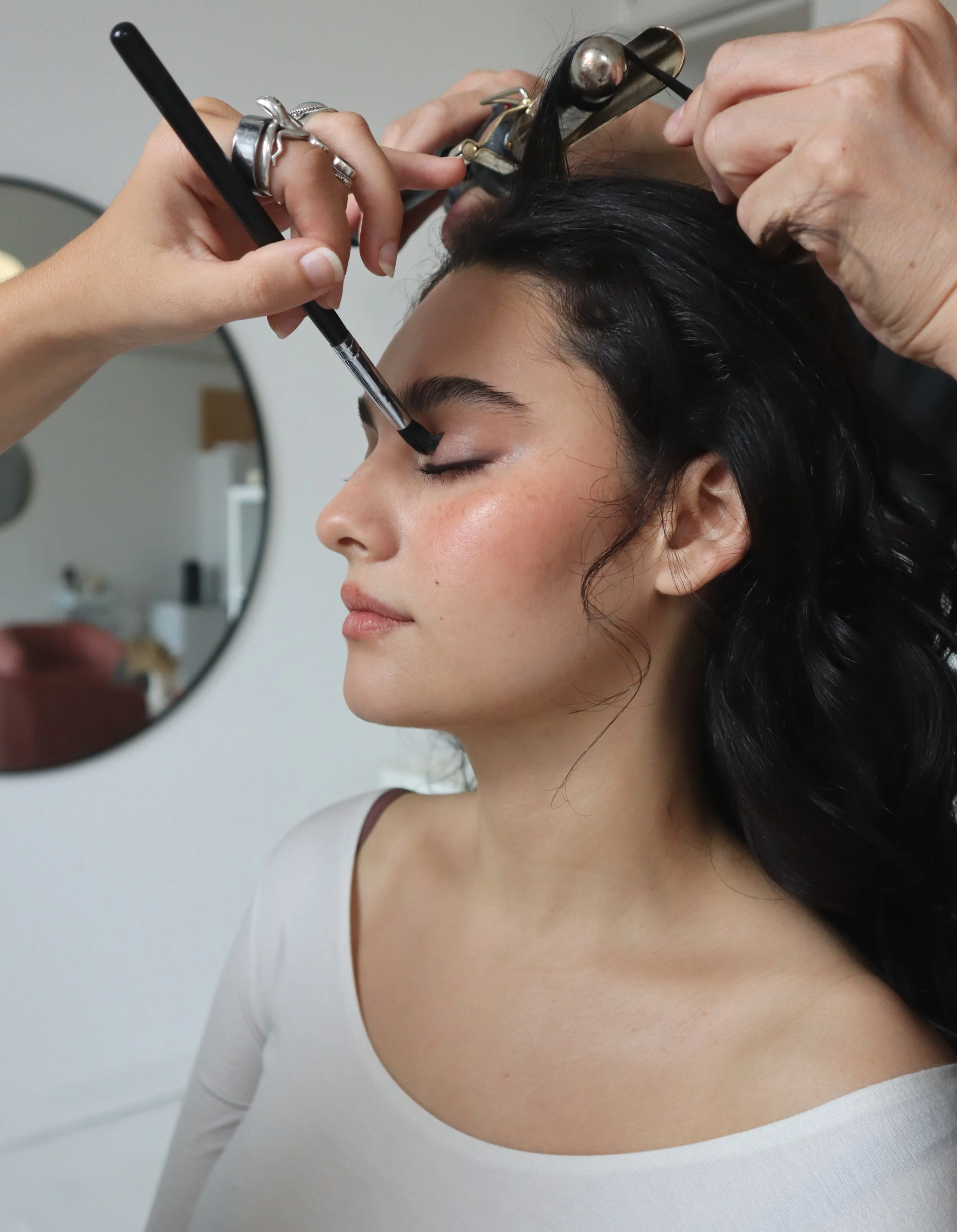 A woman getting her makeup done, with someone applying eyeshadow with a brush near her eye.