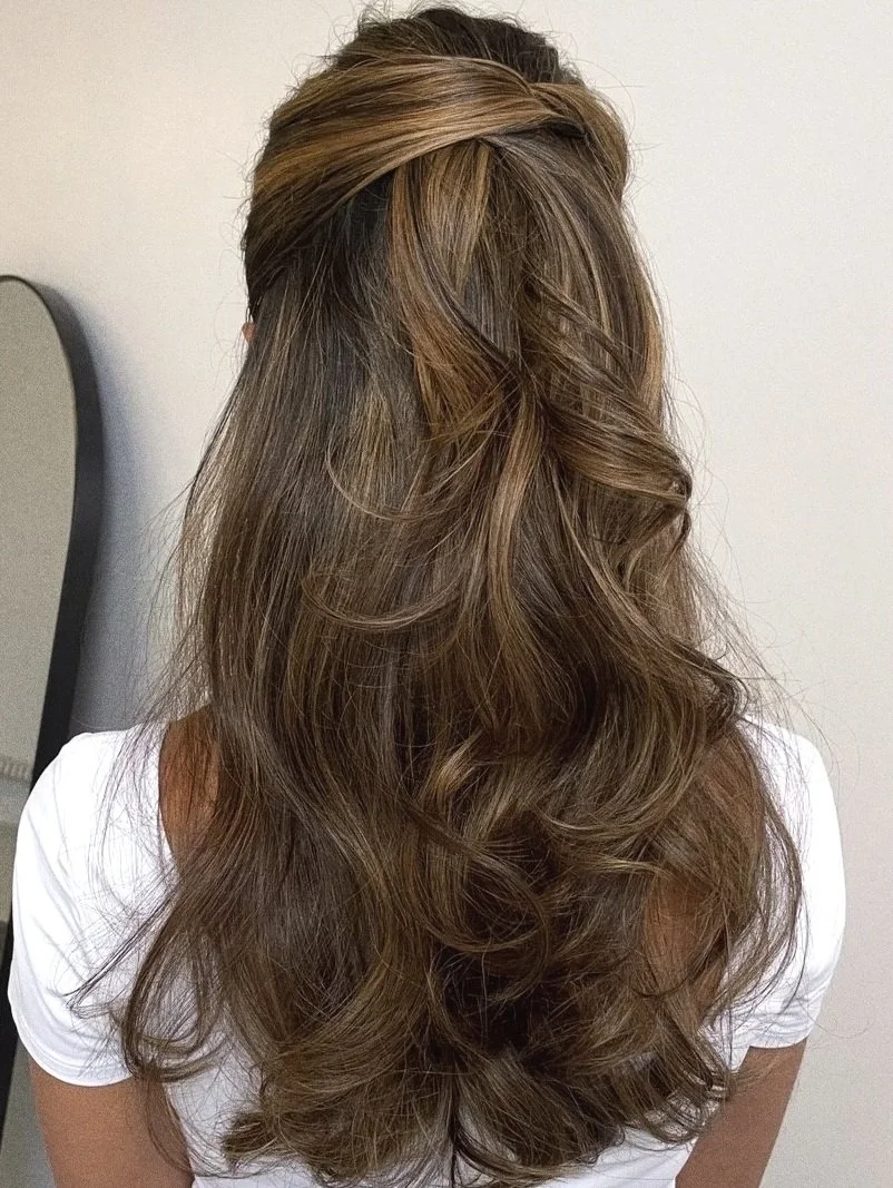 Long, layered, wavy brown hair with highlights on a woman wearing a white shirt.