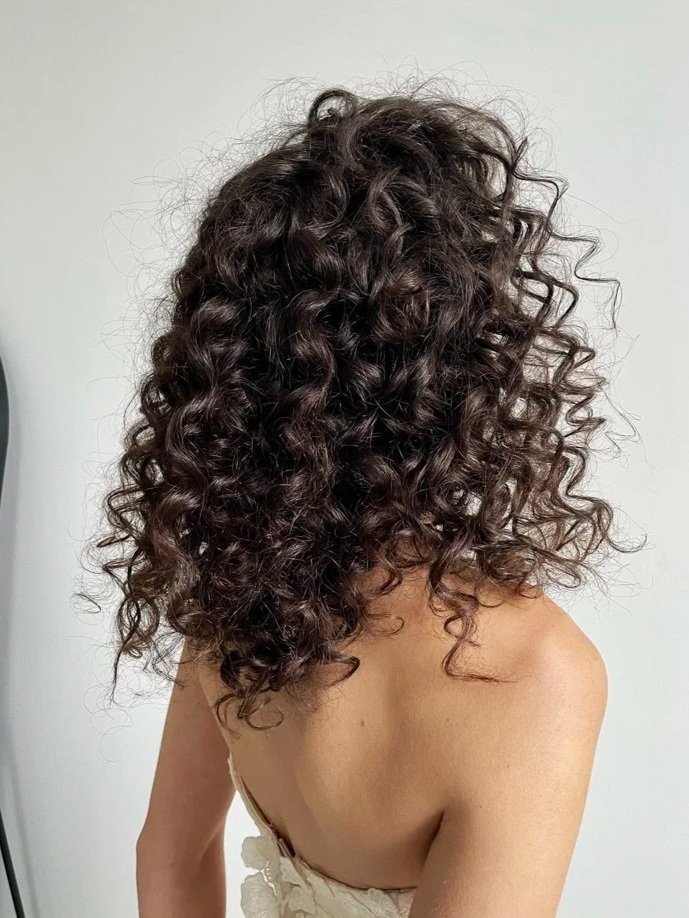 A woman with dark, curly hair covering her face, wearing a strapless top or dress.
