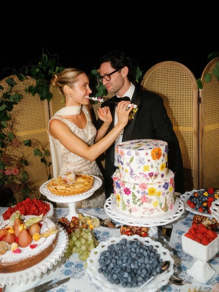 Bride and groom at their wedding cake cutting celebration with desserts and a large floral decorated cake.