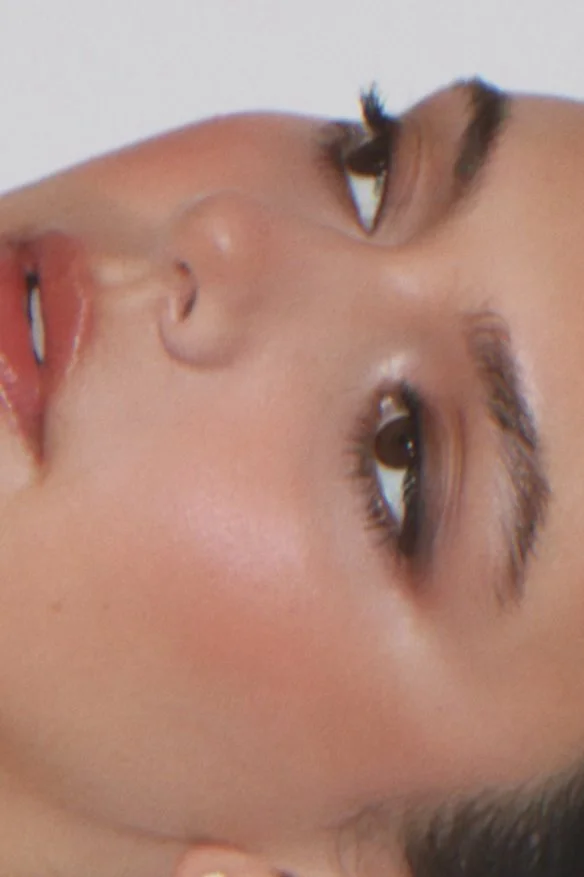 Close-up of a woman's face showing her nose, mouth, and eyes, with makeup and well-groomed eyebrows.