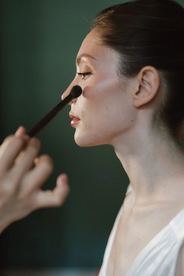 A woman with makeup being applied, focusing on her profile with a makeup brush near her eye.
