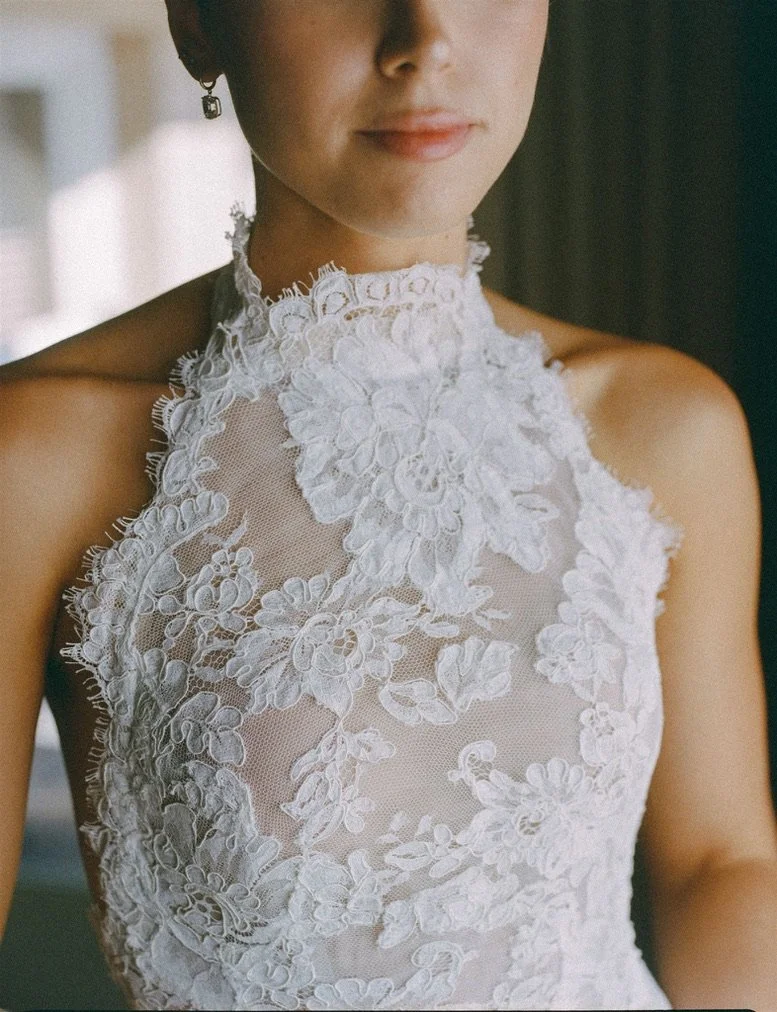 Close-up of a woman wearing a high-neck, sleeveless white lace dress with floral embroidery.