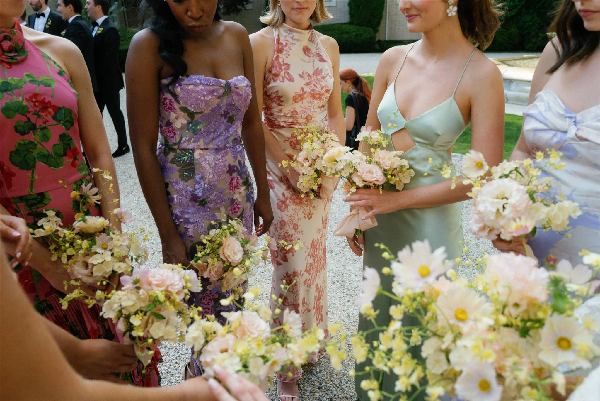 Group of women in colorful floral dresses holding bouquets of flowers at an outdoor event.
