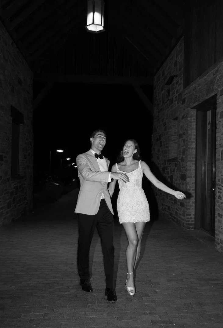 A man and woman dressed in formal attire walking and laughing at night.