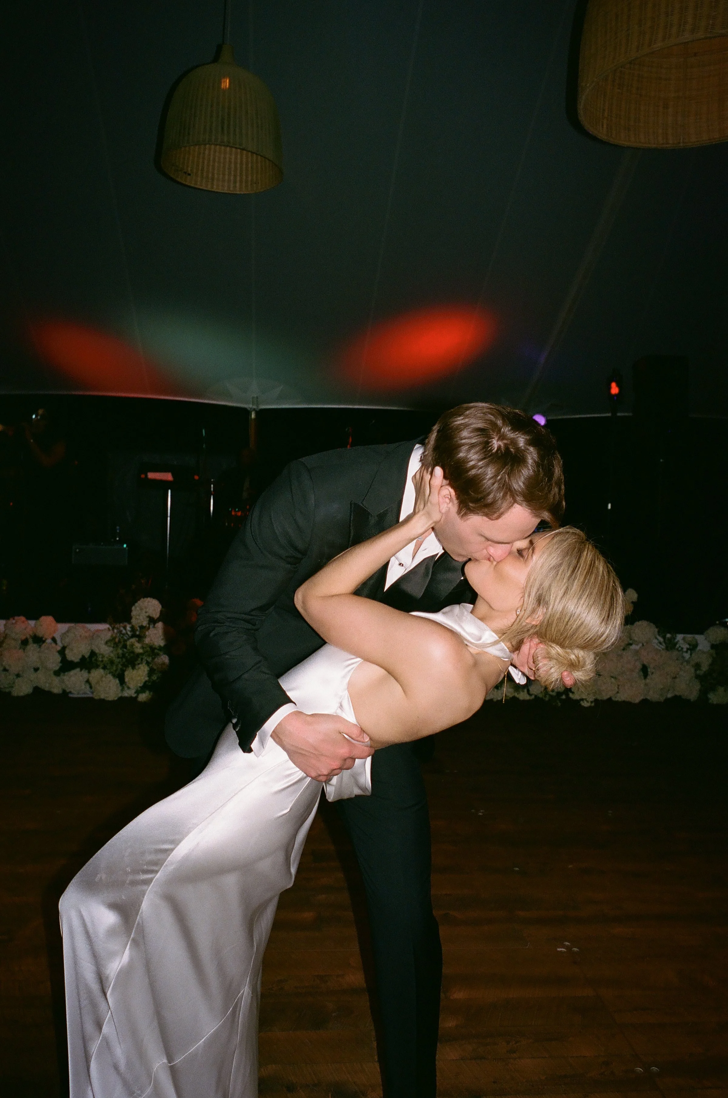 A couple kissing at a wedding reception, with the groom dipping the bride as they share a kiss on the dance floor.