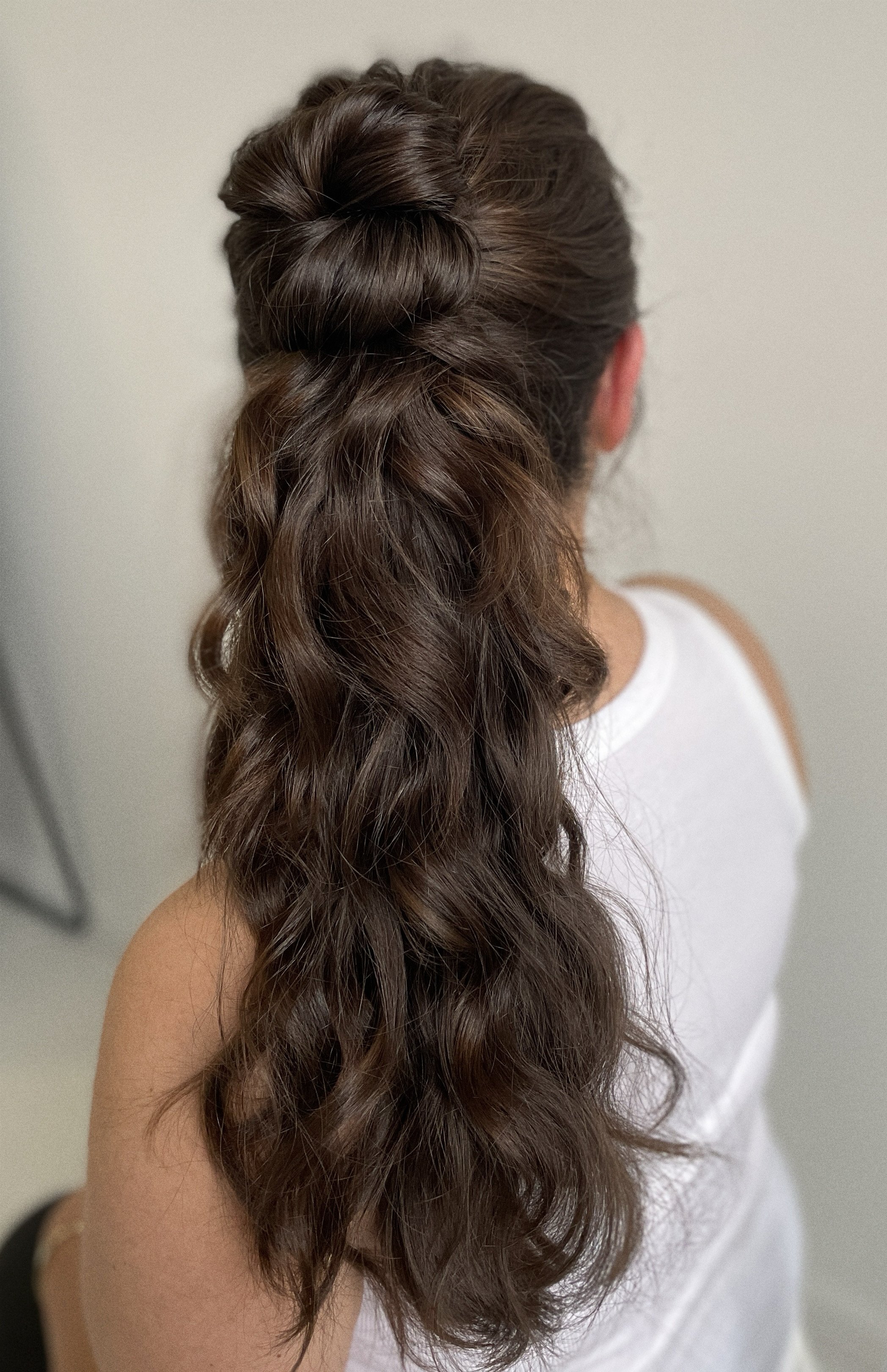 Back view of a woman with long, wavy brown hair styled in a half-up, half-down fashion.