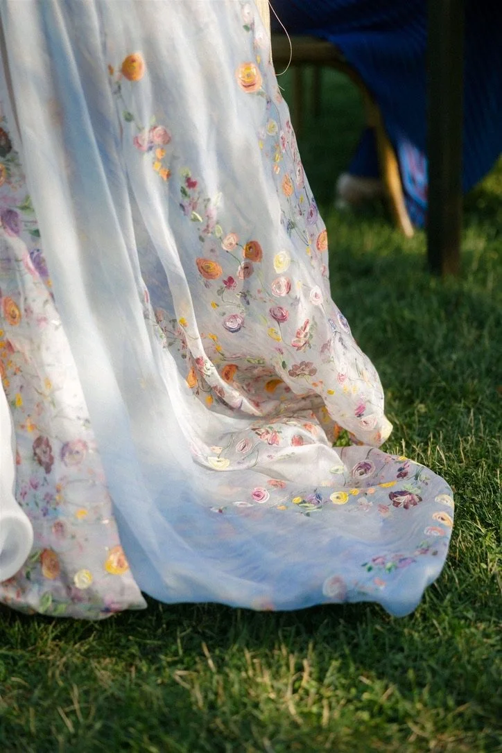 Close-up of a light, sheer fabric with embroidered colorful floral patterns, draped over grass outdoors.
