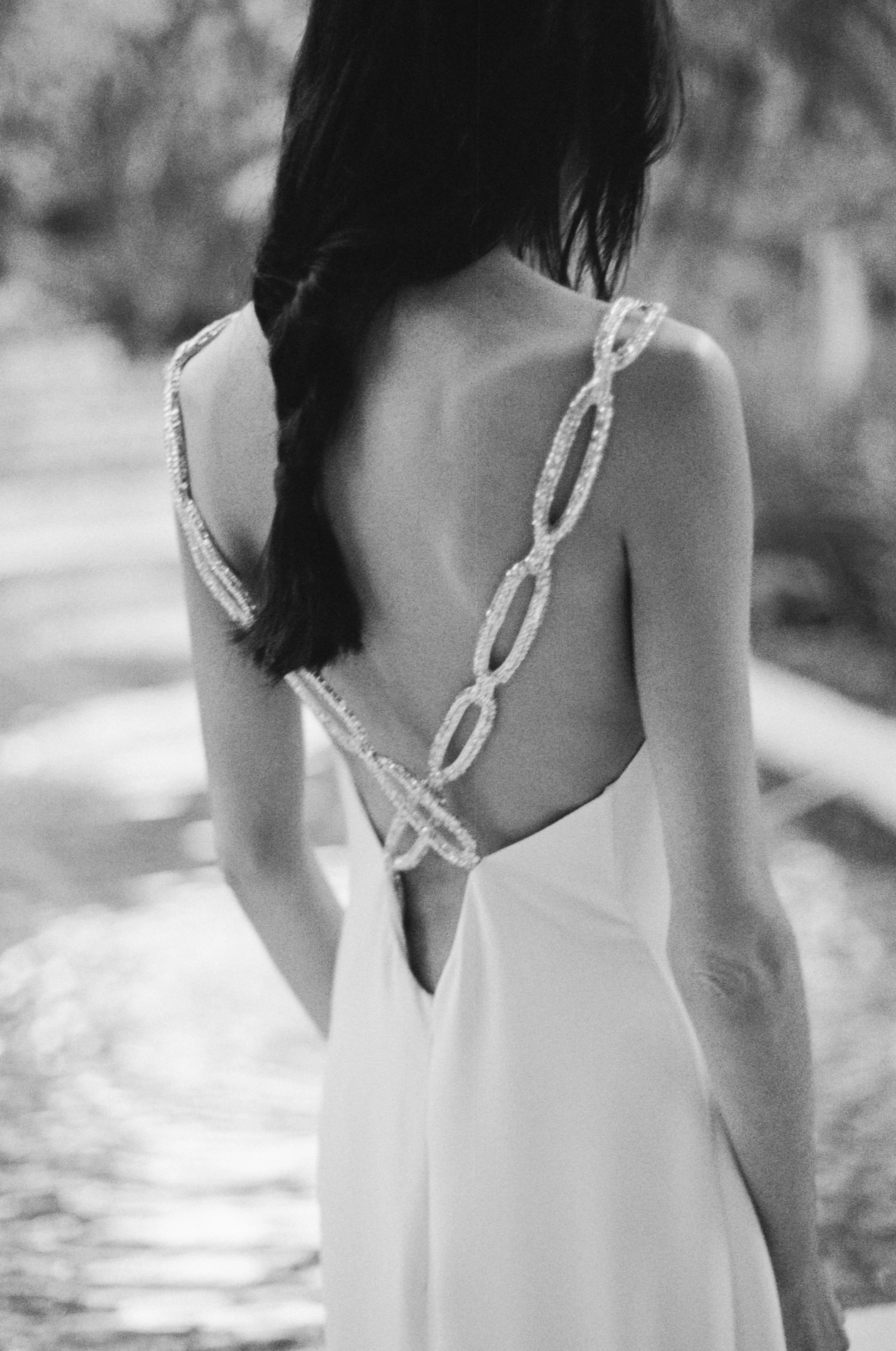 A woman in a backless dress with decorative straps standing near water, with her back to the camera wearing vintage Valentino in Mexico