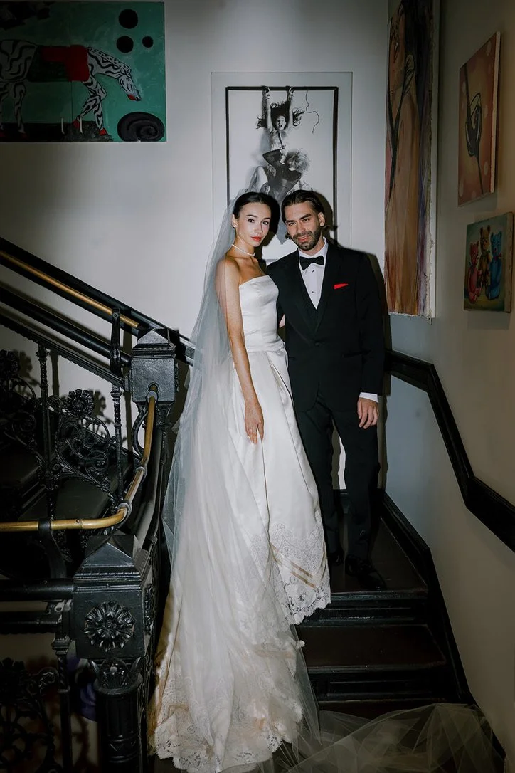 Bride and groom in formal wedding attire standing on a staircase at an art gallery, surrounded by colorful artwork on the walls.