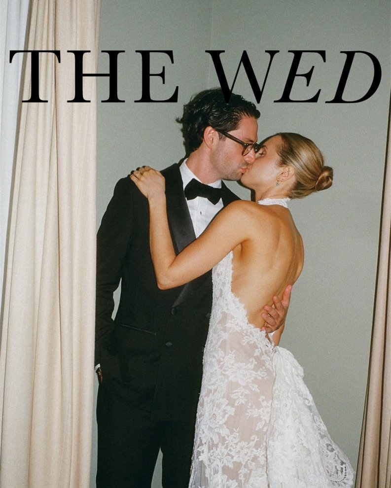 A couple dressed in wedding attire sharing a kiss, with the groom in a tuxedo and the bride in a lace wedding dress.