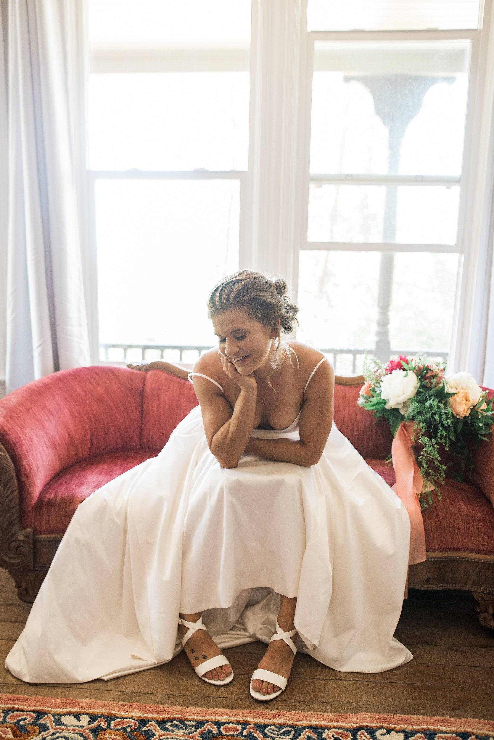 Bride seated on a red velvet chair in her wedding gown, featuring soft updo and natural bridal makeup by Spokane wedding hair and makeup artist Terri Reece.