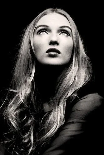 Black and white portrait of a young woman with long, wavy hair gazing upward.