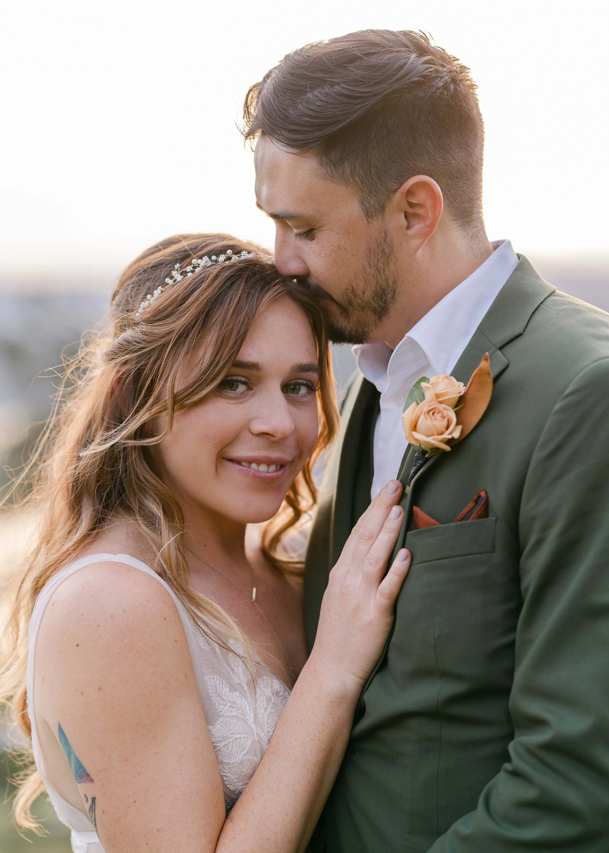 Bride and groom embracing outdoors, bride styled with loose waves, glowing makeup, and delicate floral accents by Spokane and Coeur d’Alene bridal hair and makeup artist Terri Reece Studios.