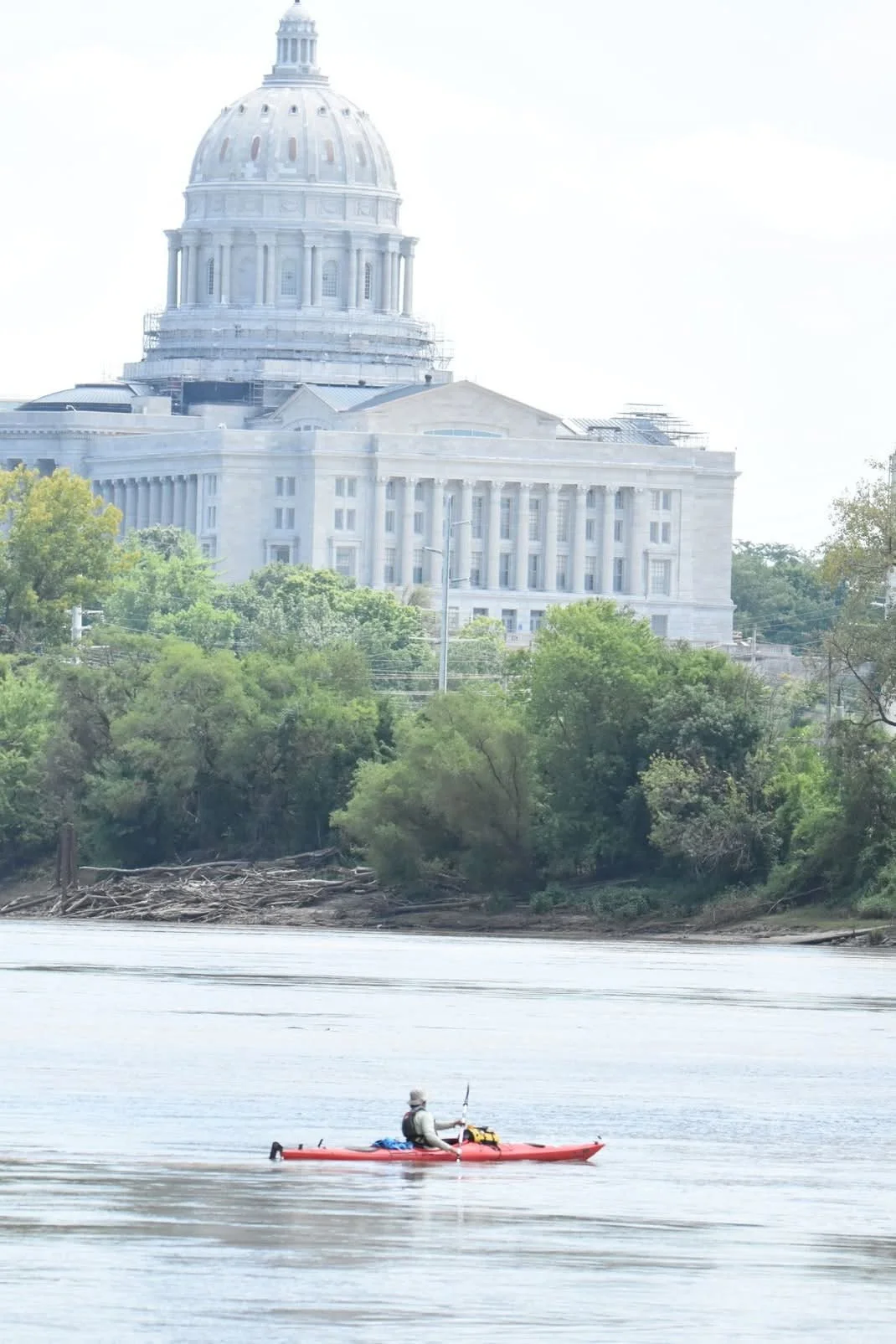 A person kayaking on a river with the state capitol building in the background.