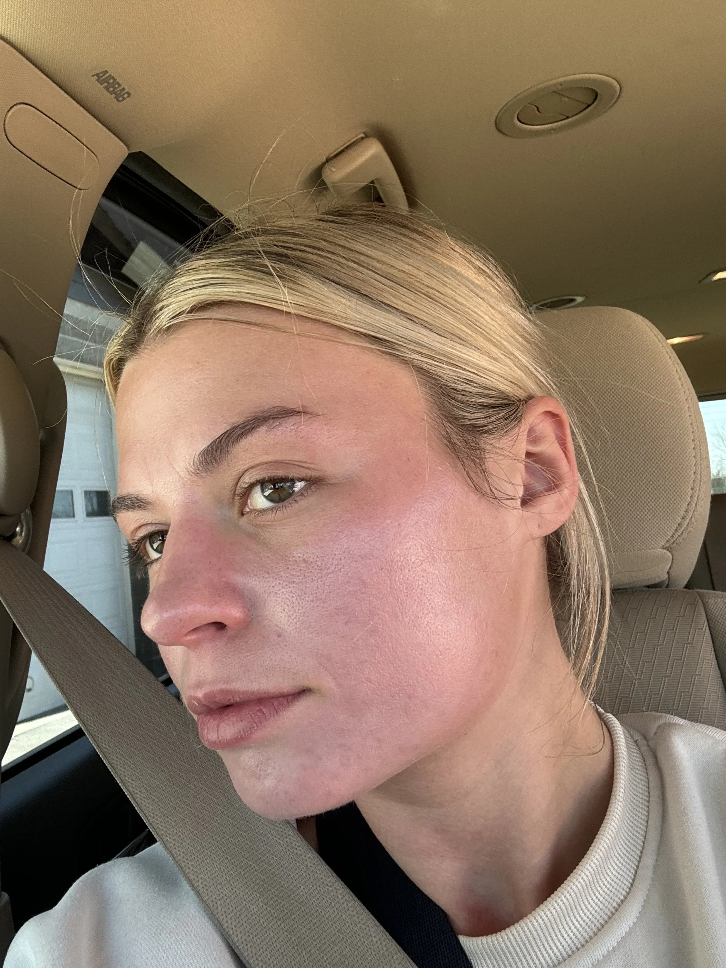 Close-up of a woman with fair skin and blonde hair sitting in a vehicle, wearing a seatbelt.