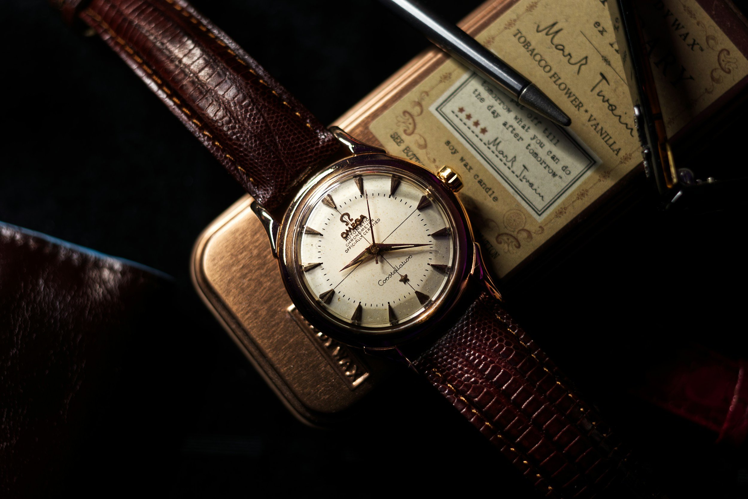 A vintage Omega wristwatch with a leather strap resting on a metal box.
