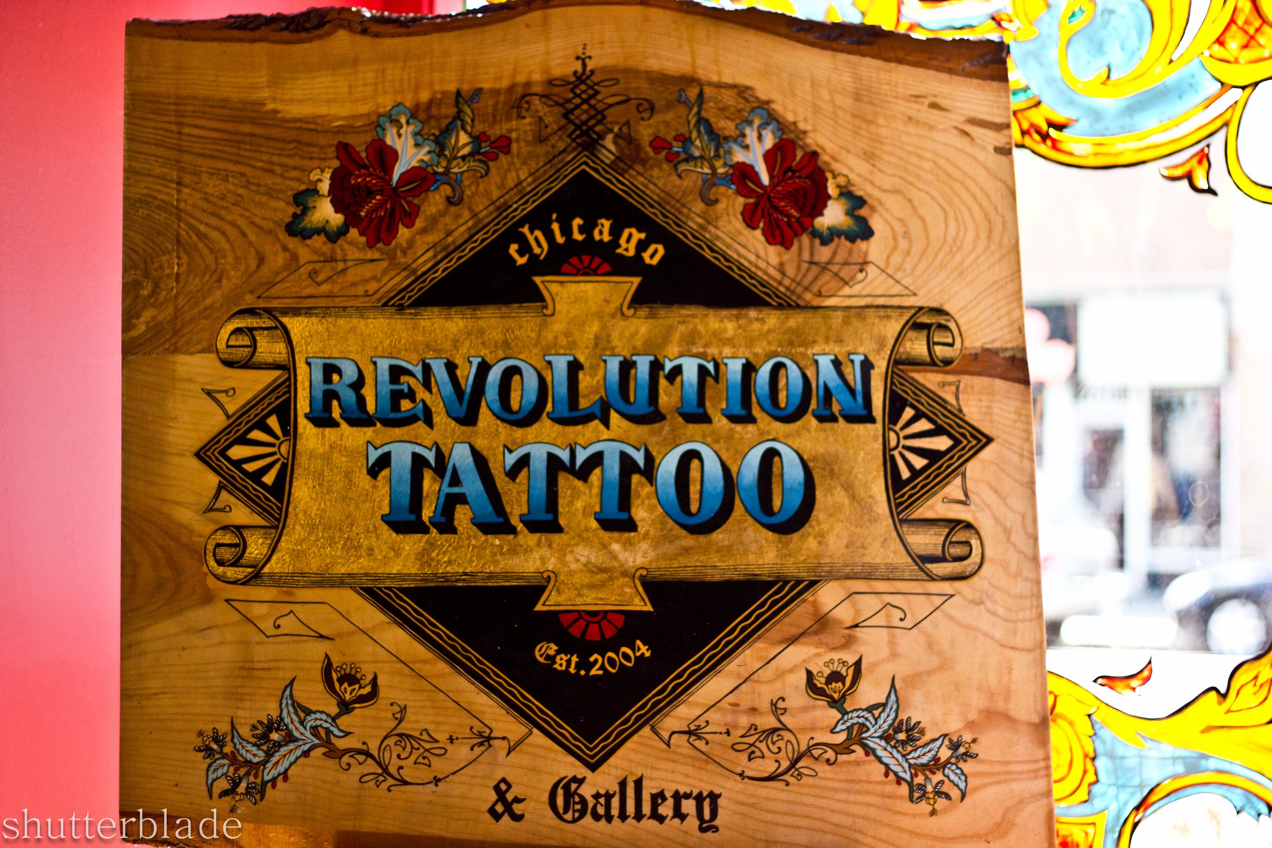 Wooden sign for Revolution Tattoo, established in 2004, located in Chicago, with decorative floral and geometric designs.