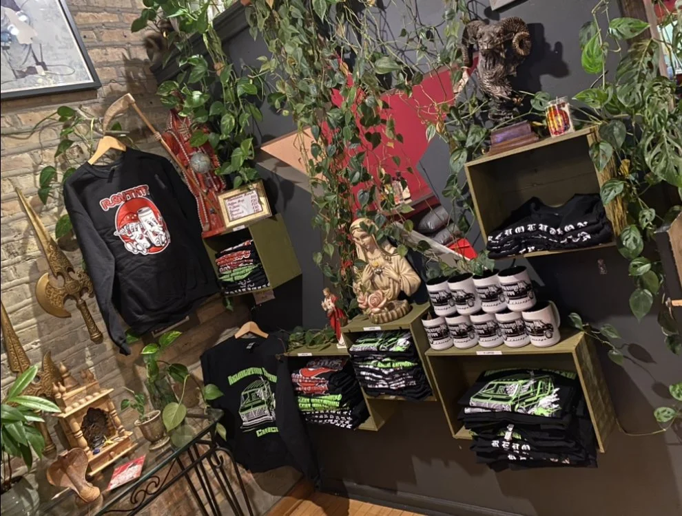 Display of Halloween-themed merchandise including hoodies, t-shirts, mugs, and accessories, decorated with green plants and Halloween decorations.