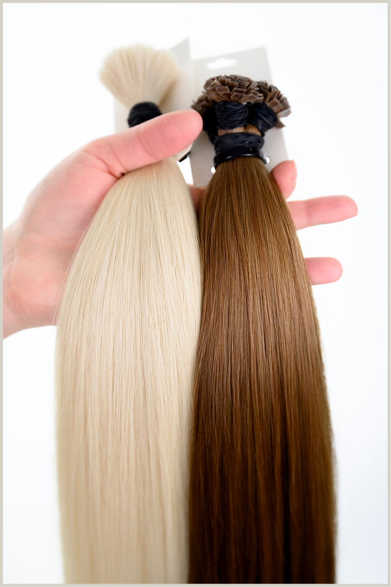 a hand holding two bundles of hair extensions in brown and blonde on white background