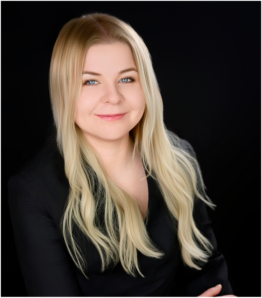 woman smiling with long blonde hair wearing a black top and with a black background