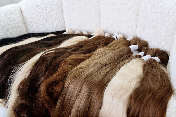 a whole pile of coloured hair extension bundles laid out on a white sofa chair