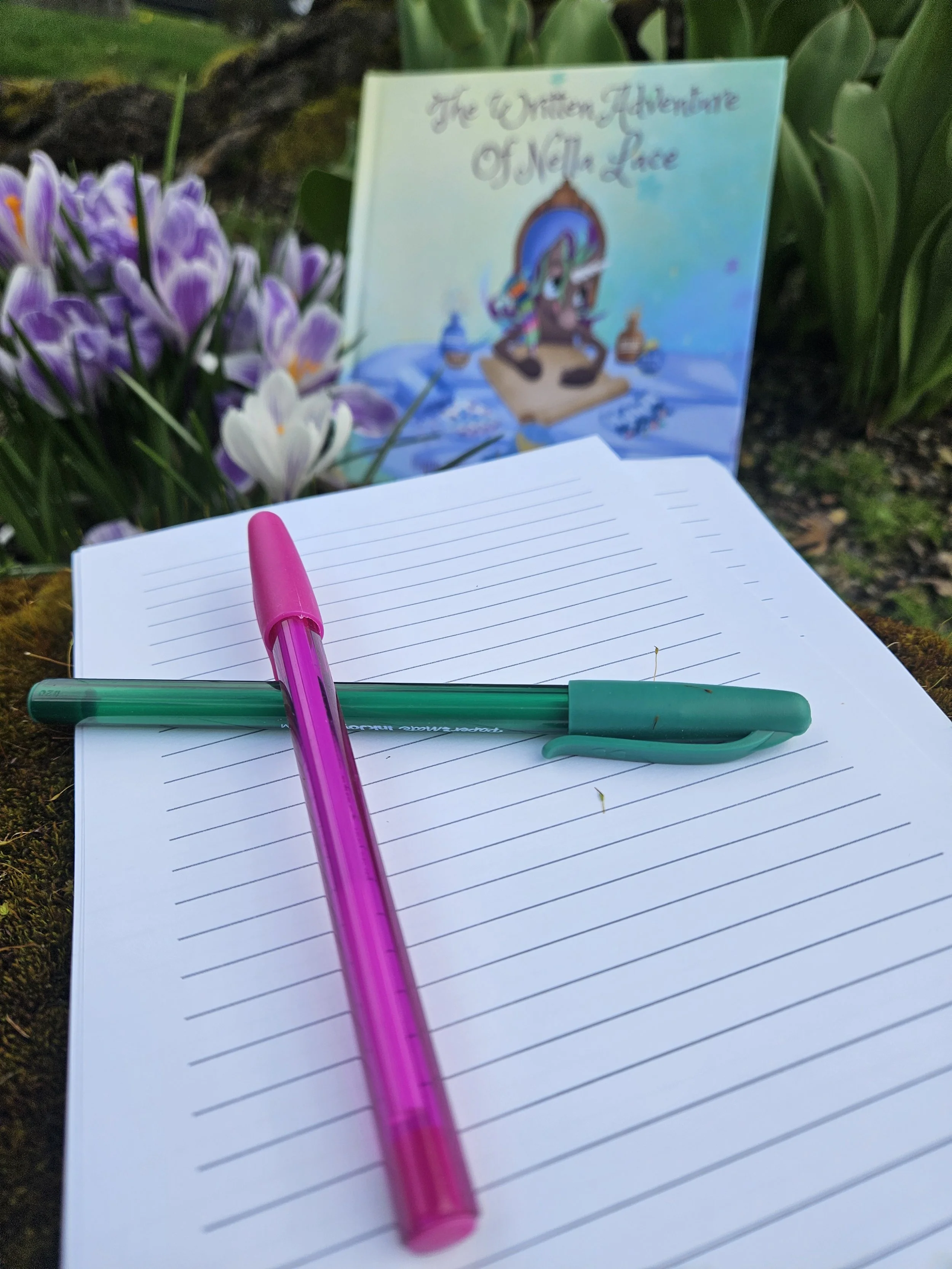 Stationary and pens take up the foreground with crocus and The Written Adventure of Nella Lace out of focus in the background