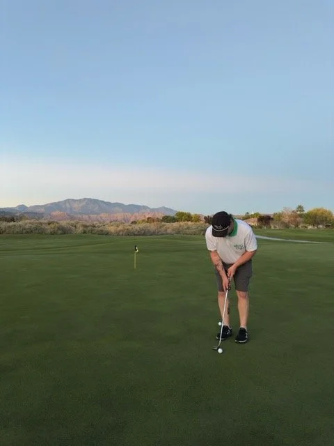 A person playing golf on a green course with mountains in the background