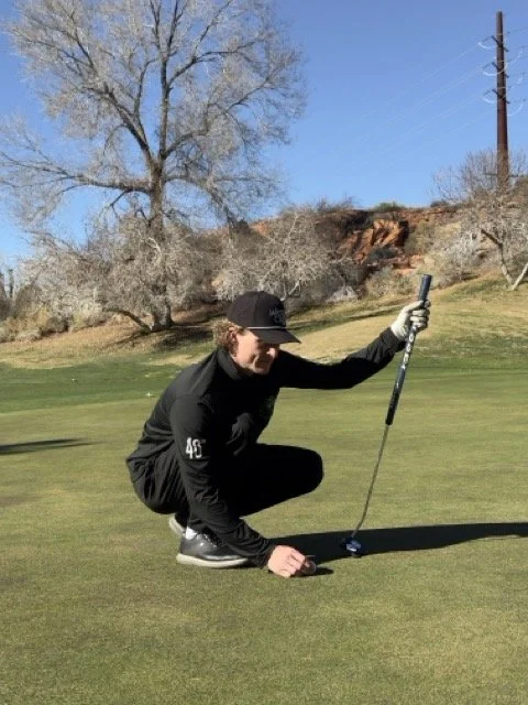 Person crouching on a golf course, holding a golf putter and preparing to putt.
