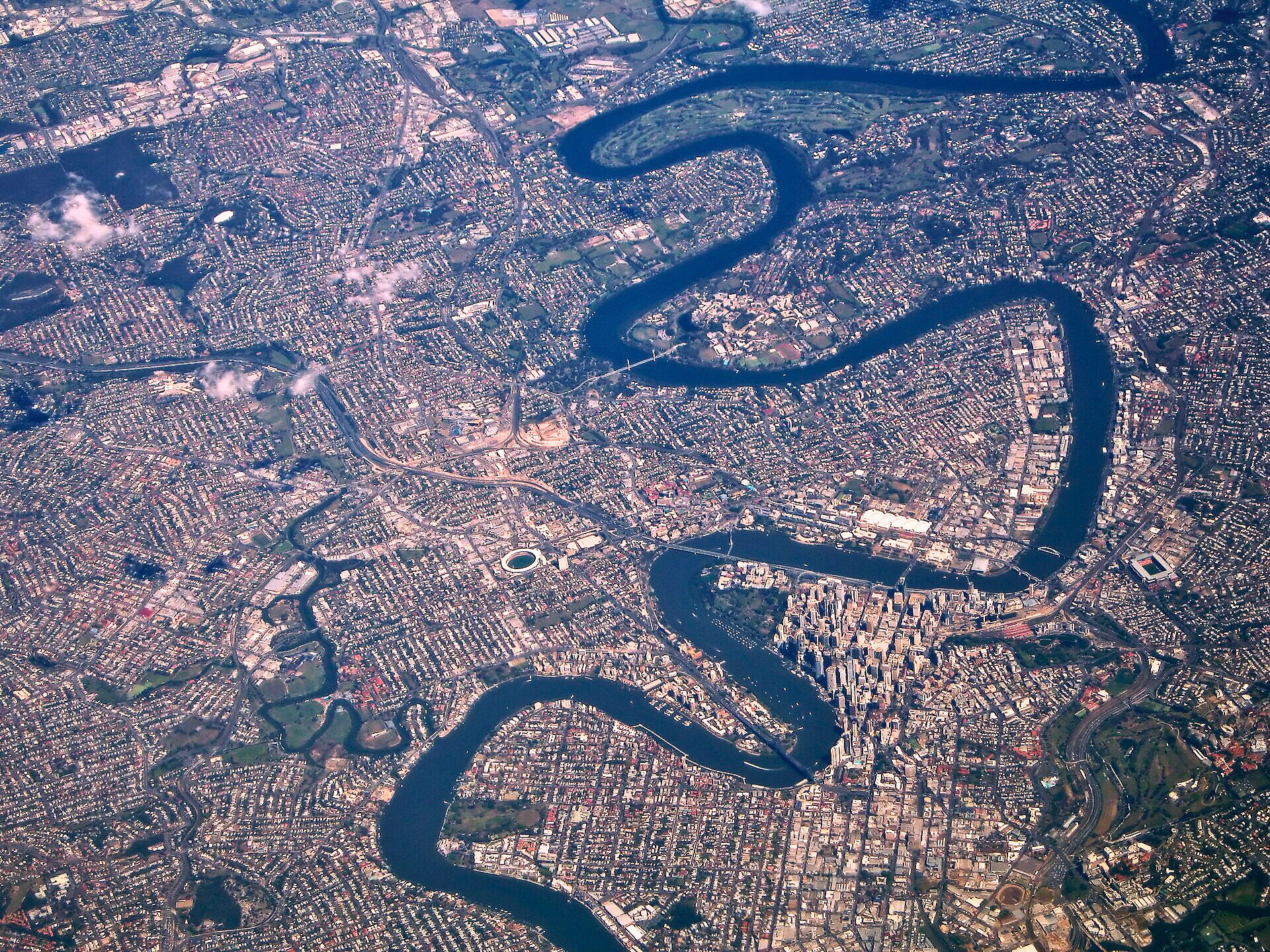 An aerial view of a city with a meandering river running through it, showing dense urban development, bridges, and green spaces.