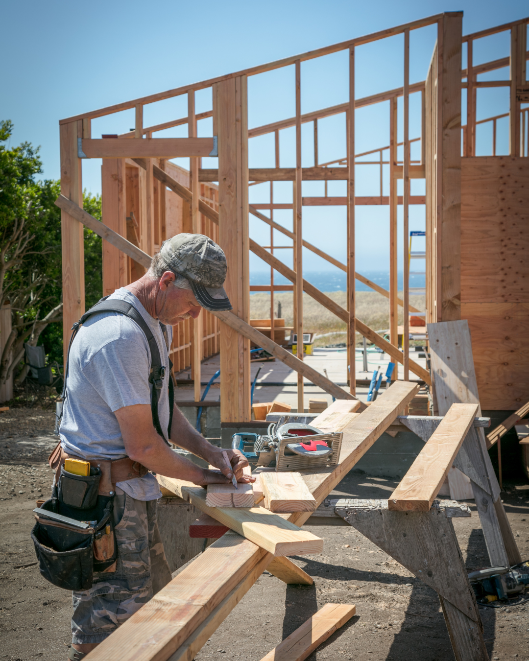 builder marking a wood plank with a houseframe in the background