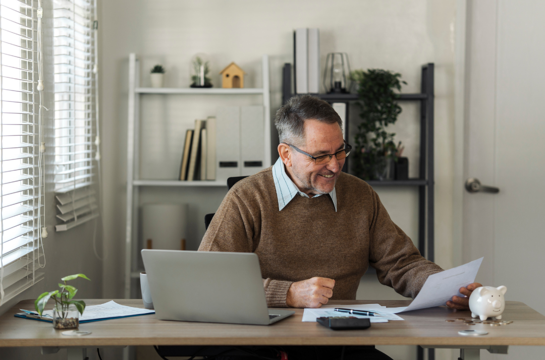 A person infornt of a laptop smiling while review a paper document in their hand