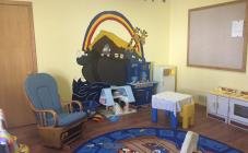 Living room with blue armchair, wooden sofa, and a black piano. There are various decorations, photographs, and a rainbow decal on the wall.