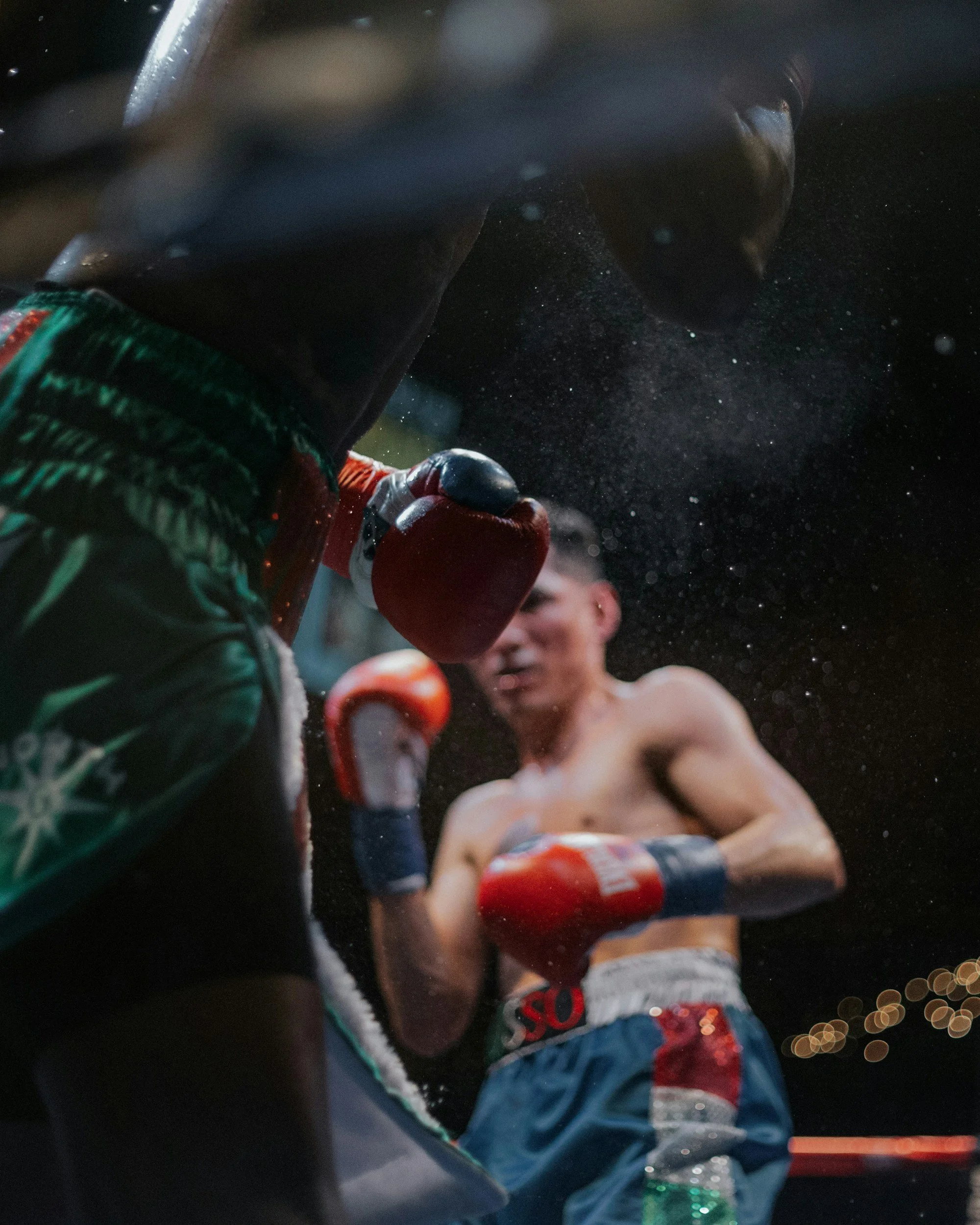 A boxer wearing red gloves and shorts is preparing to punch before a match, while the referee is holding a water bottle. The scene is dark, with water spray visible in the air.
