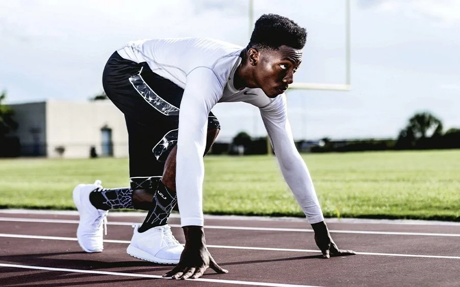 Male athlete in starting position on a track field, preparing for a race.