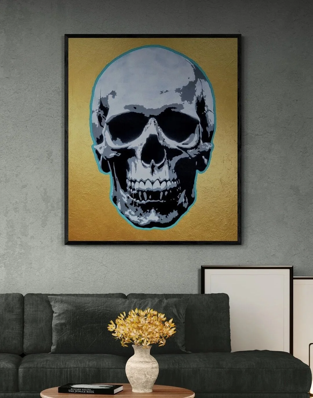 A framed artwork of a skull on a gold background hanging on a textured gray wall above a dark gray sofa with mustard-colored cushions placed on it, in a living room setting.