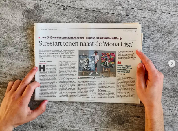 A person holding a folded newspaper on a wooden surface, with both hands visible.