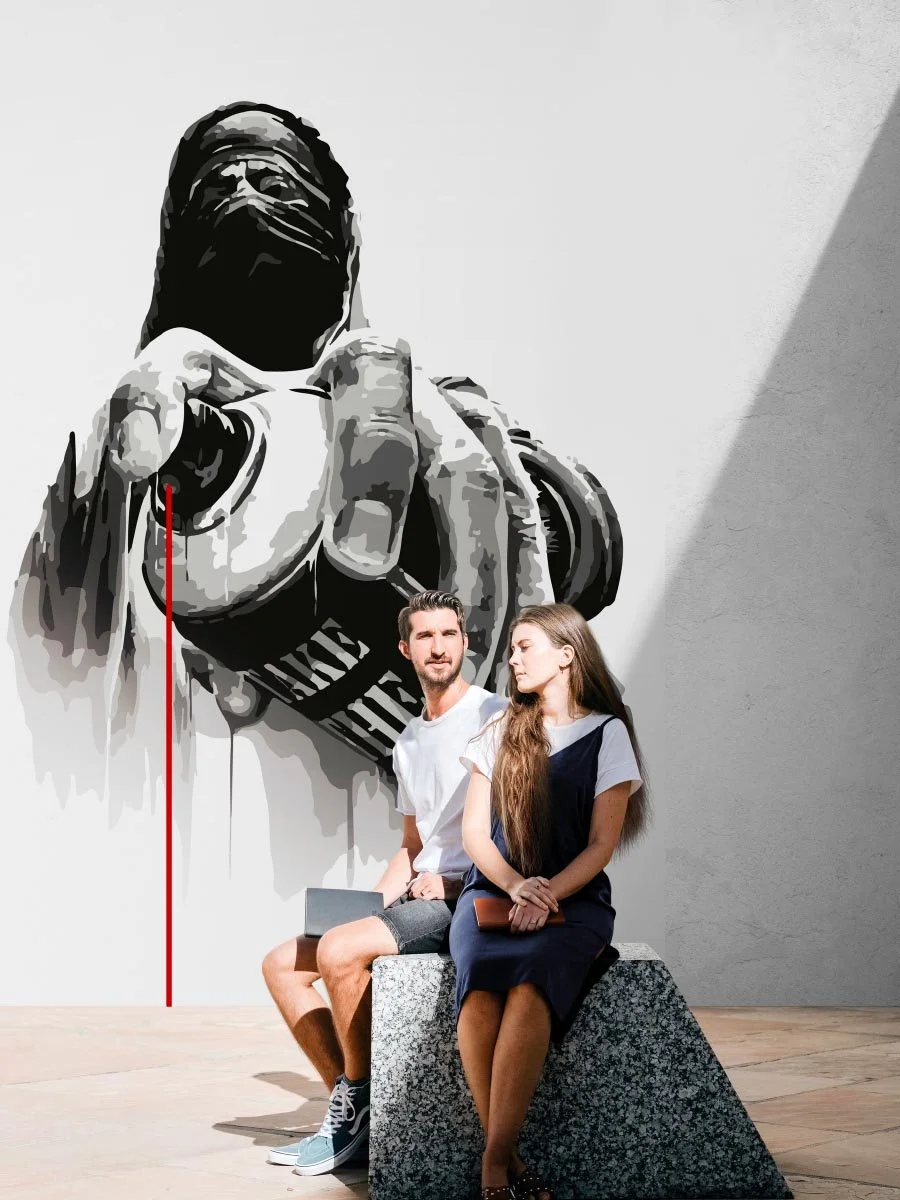 Two people, a man and a woman, sitting on a stone block in an art gallery in front of a large black and white wall sculpture of a hand pointing at the viewer.