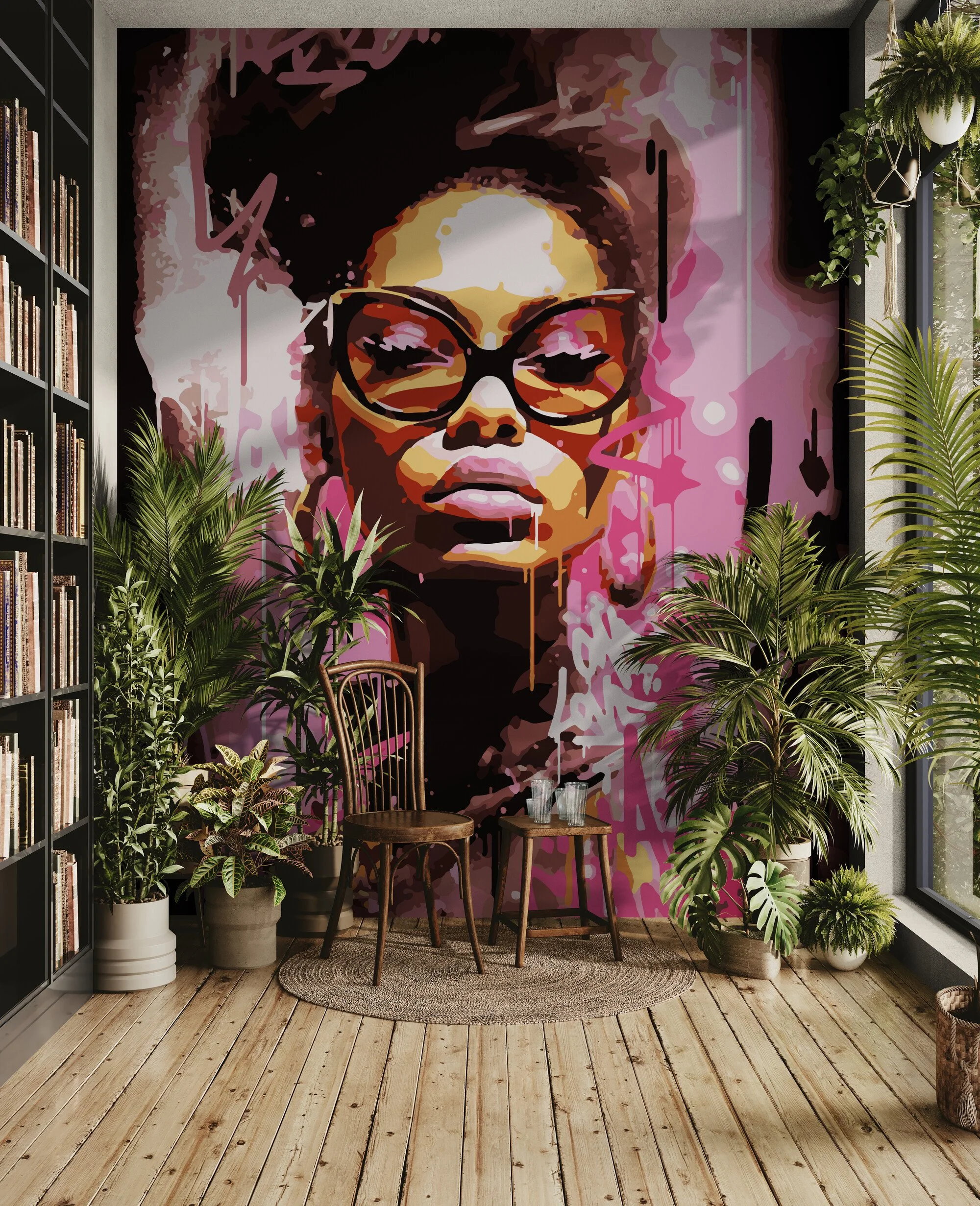A large pink and black mural of a woman wearing sunglasses decorates a wall in a cozy room. The room has wooden floors, multiple potted plants, a small round rug, and two wooden chairs with a small glass of water on one of them. There is a bookshelf filled with books on the left and large windows on the right providing natural light.