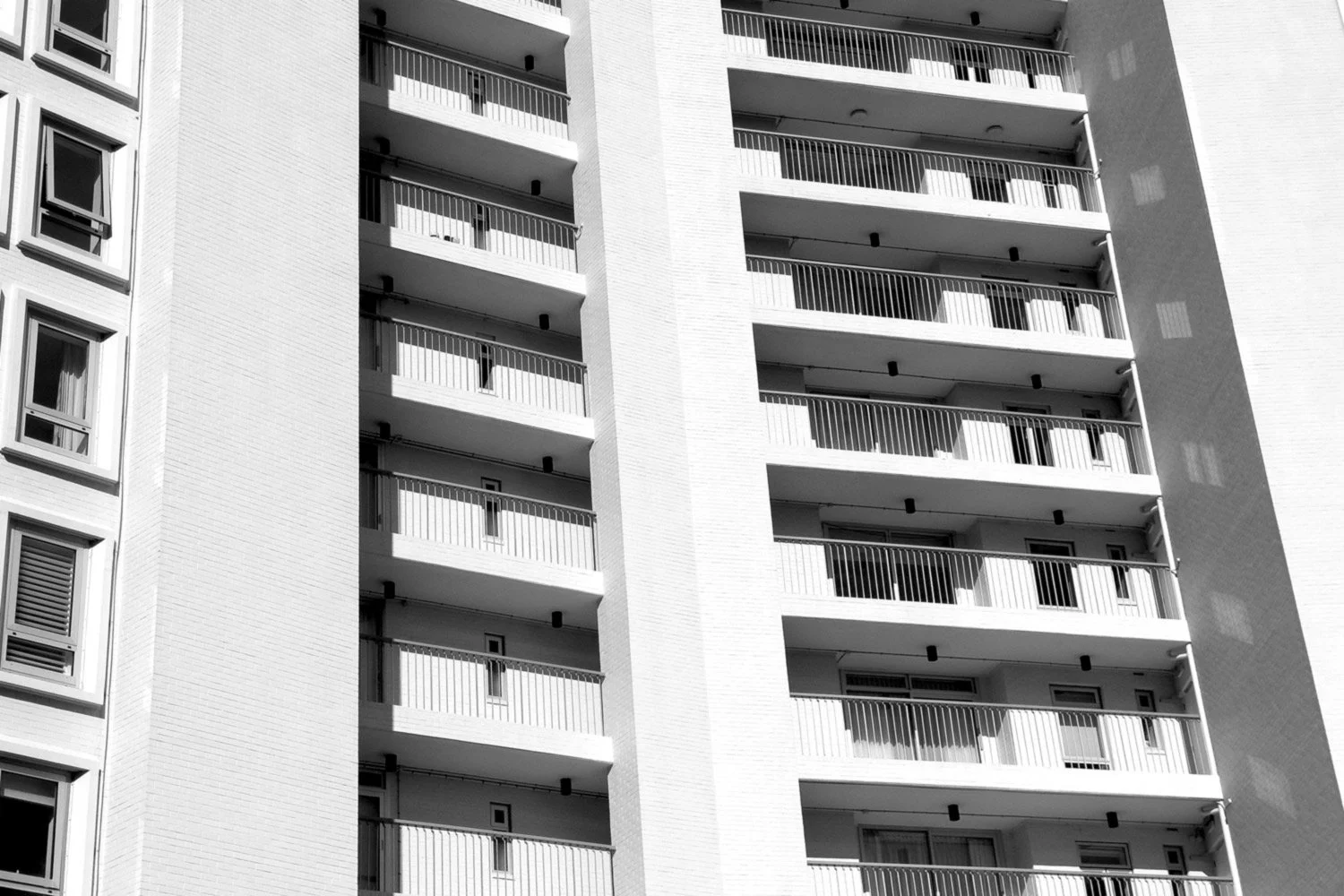 Black and white modernist photo of a high-rise apartment building with multiple balconies.